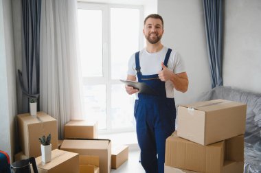 Üniformalı bir adam elinde bir pano tutuyordu. Etrafı yeni, parlak bir dairede kutuları taşırken başparmaklarını kaldırıyordu.