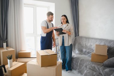 Taşındığı gün yeni bir dairede karton kutularla bir belgeyi imzalayan kadın müşteriye yardım eden bir servis çalışanı taşınıyor.