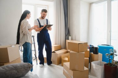 Kadın üniformalı bir adamla konuşuyor. Etrafı karton kutularla çevriliyken taşınma gününün detaylarını tartışıyor.