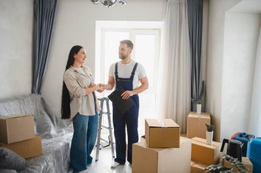 Ev sahibi ve profesyonel nakliyeci, taşınan kutularla dolu bir odada güven ve başarılı yer değiştirme hizmetlerini sembolize ederek el sıkışıyor.