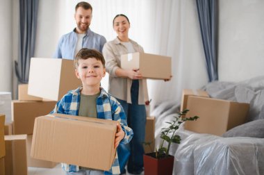 Aile, oturma odasında karton kutu paketliyor, gülümsüyor ve yeni bir mülke taşınıyor, mutluluk ve hayaller gösteriyor.