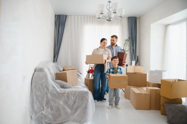 Mutlu aile yeni bir dairede eşyalarını boşaltıyor. Ebeveynler ve oğulları karton kutular taşıyorlar, yeni evlerine taşınıyorlar.