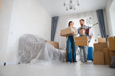 Ebeveynler ve çocuklar birlikte yeni bir daireye taşınıyorlar. Karton kutular ve bir bitki taşıyorlar. Paketleri açmaya hazırlar.