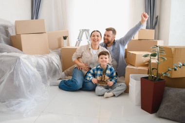 Mutlu bir aile, oğlu yerde oturuyor. Etrafı kutularla çevrili. Yeni dairelerine taşınmalarını kutluyorlar.