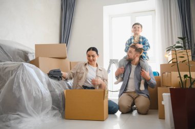 Mutlu ve çocuklu bir aile taşınan kutularla çevrili yeni bir dairede kişisel eşyalarını boşaltarak eğleniyor.