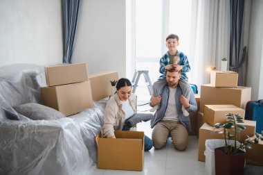 Yeni bir eve taşınıp yeni bir hayata başladıktan sonra karton kutulardan eşyalarını çıkaran mutlu bir aile.
