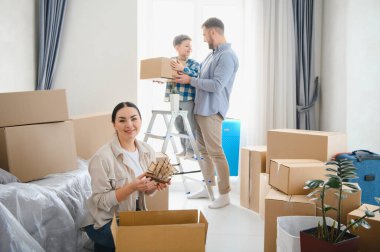 Parlak, modern bir dairede karton kutuları açıp taşınmayı kutlayan mutlu bir aile.