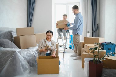 Aile yeni evlerinde taşınan kutuları açıyor. Ebeveynler ve çocuklar taşınmayı ve yeni başlangıçları sembolize ederek nesneleri düzenlemekle meşguller.