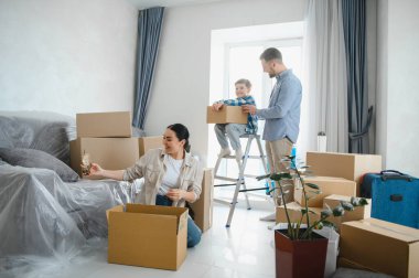 Aile yeni bir dairede kutuları açıyor, ebeveynler ve çocuklar birlikte çalışıyor, taşınma günü, taşınma.