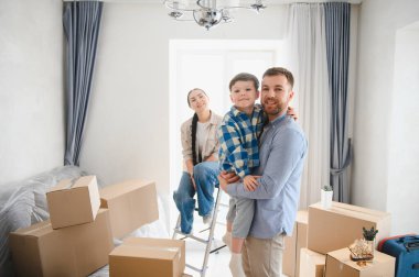 Karton kutularla çevrili yeni bir dairede gülümseyen aile, taşınmanın heyecanını kutluyor.