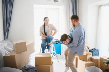 Ebeveynler ve oğulları, yeni boş dairelerinde, karton kutuların arasında oyun oynuyorlar, taşınmanın zevkini yaşıyorlar.