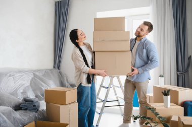 Mutlu çift boş daireye taşınıyor, karton kutuları taşıyor, taşınma gününü ve yeni bir başlangıcı kutluyorlar.