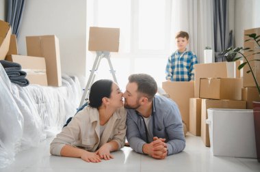 Mutlu bir aile yeni bir daireye taşınıyor, taşındıktan sonra karton kutularla çevrili yerde yatıyor.