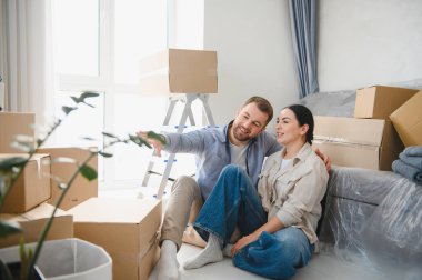 Genç çift, yeni apartmanlarında karton kutuların arasında oturuyor, gülümsüyor ve ilk evlerinde rahat geleceklerini planlıyorlar.