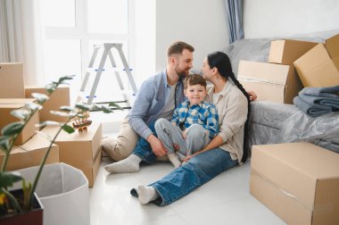 Yeni evlerinde karton kutularla çevrili küçük oğlu yerde dinlenen mutlu bir aile.