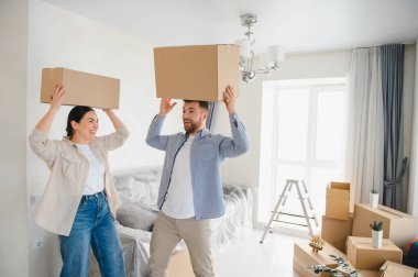 Mutlu çift yeni evlerine taşınmayı kutluyor. Karton kutuları parlak, modern bir odada taşıyorlar.