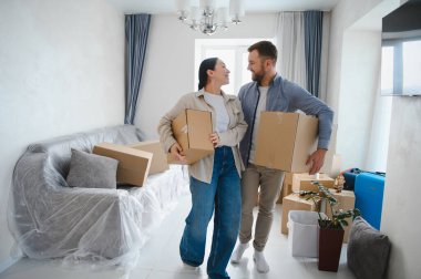 Yeni dairelerine kutuları taşıyan genç bir çift birlikte mutlu bir başlangıç yaparken gülümsüyorlar.