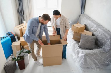 Genç çift eşyaları büyük bir karton kutuya yerleştiriyor ya da paketliyor. Ev taşınmasına hazırlanıyorlar. Koruma için sarılı kanepe