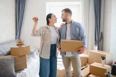 Gülümseyen genç çift yeni daireye taşınıyor, ellerinde anahtarlar ve karton kutular, heyecanlı ev sahipleri yeni bir hayata başlıyorlar.