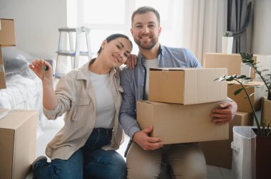 Genç bir çift yeni bir eve sahip olmayı kutluyor, ellerinde anahtarlar ve karton kutular var. Yerleştirme ve emlak konsepti