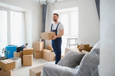 Önemli bir taşınma kutusunu teslim ederken gülümsüyor, yeni bir daireye ya da eve eşyalarını yerleştiriyor.