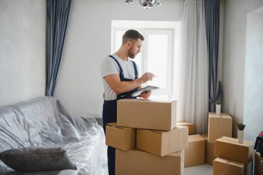 Profesyonel nakliyeci boş bir odada duruyor, karton kutularla çevrili bir panoyu yeniden yerleştirmek için kontrol ediyor.