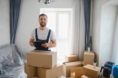 Üniformalı, karton kutular arasında yığılmış bir pano ile gülümseyen, bir yerleşim yeri değiştirme servisi hazırlayan ve düzenleyen