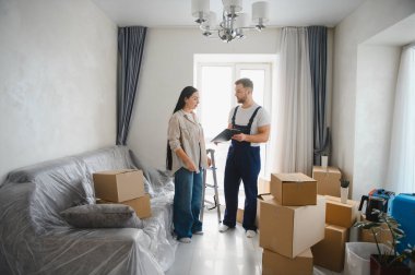 Profesyonel bir nakliyeci bir kadınla konuşuyor, taşınma detaylarını tartışıyor ve mukavva kutularla çevrili belgeleri imzalıyor.