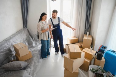 Yeni bir dairede karton kutularla çevrili bir kadın ve taşınan bir servis çalışanı listeyi birlikte kontrol ediyorlar.