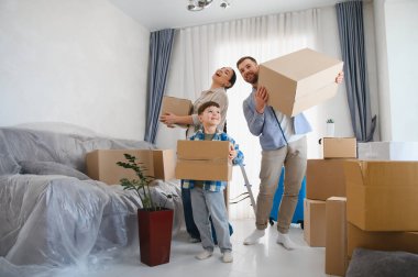 Yeni bir dairede gülümseyen ve karton kutular tutan genç bir aile başarılı bir taşınmayı kutluyor.