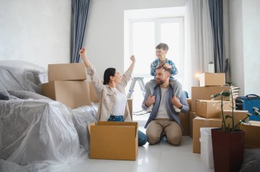 Genç bir aile taşınma gününü kutluyor, eşyalarının paketini açıyor ve çocuklarıyla birlikte yeni dairenin tadını çıkarıyor.