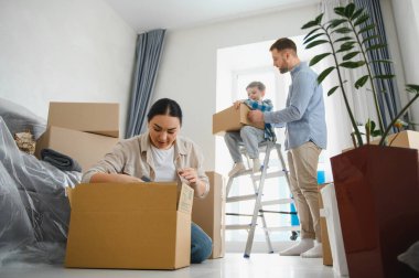 Mutlu bir aile yeni bir eve taşınıyor, aileler ve çocuklar kutuları açıyor ve eşyaları birlikte düzenliyorlar.
