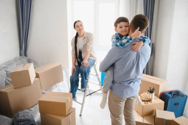 Mutlu bir aile yeni bir daireye taşınıyor. Ebeveynler ve çocuklar taşındıktan sonra karton kutularla çevrili duruyorlar.