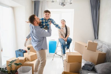 Mutlu aile yeni bir evde kutuları açıyor, baba kucağında oğlu, anne oturuyor, yeni apartman hayatının tadını çıkarıyor.