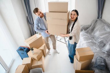 Genç ve mutlu bir çift, yeni evlerine ya da evlerine taşınmalarını kutlayan bir yığın karton kutu taşıyor.