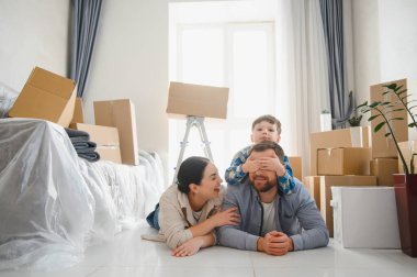 Karton kutularla çevrili yerde yatıp yeni evlerinde eğlenen mutlu bir aile.