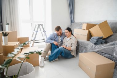 Genç bir çift, karton kutularla çevrili yeni apartman planlarını tartışıyor ve taşınmaya hazırlanıyor.