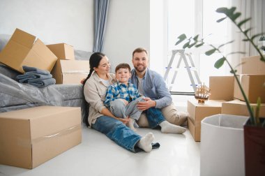 Gülümseyen aile, karton kutuların arasında oturmuş, taşınmayı ve yeni bir başlangıç yapmayı kutluyorlar.