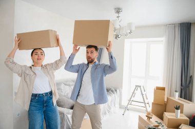 Genç mutlu çift yeni bir eve taşınmayı kutluyorlar, kafalarında kutuları taşıyorlar. Yeni evin tadını çıkarıyorum.