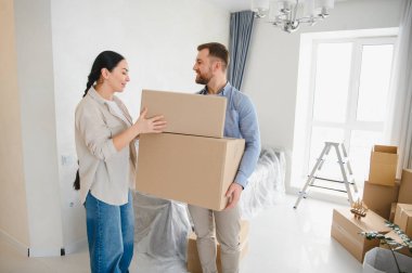 İşbirliği yapan genç bir çift, yeni boş dairelerine kutu taşıyorlar, taşınma ve mülk sahipliğini kutluyorlar.