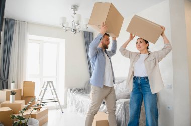 Yeni başlangıçları kutlayan genç bir çift yeni evlerinde karton kutular taşırken, etrafları erzakla çevriliyken.