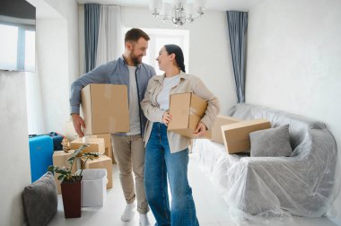 Genç çift karton kutular taşıyor, gülümsüyor ve yeni evlerine taşınırken birbirlerine bakıyorlar.