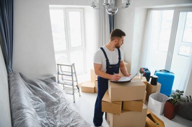 Üniformalı bir işçi panoya yazı yazıyor, apartman dairesinin taşınması için kutuları ve kişisel eşyaları düzenliyor.