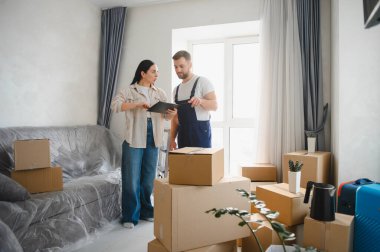 Genç bir kadın, içi karton kutularla dolu boş bir dairede profesyonel bir nakliyeci ile evrak işlerini tartışıyor.