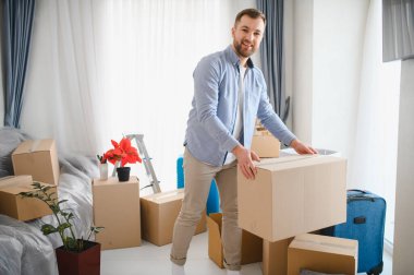 Karton kutular taşırken gülümseyen genç bir adam. Taşınma, boşaltma ve yeni bir apartman dairesine yerleşmek.