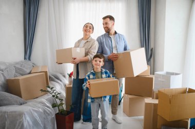 Yeni evlerinde gülümseyen ve karton kutular taşıyan üç kişilik bir aile taşınmayı ve yeni bir başlangıç yapmayı kutluyorlar.