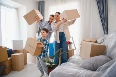 Mutlu aile yeni evlerinde karton kutuları açıyor. Aileler ve oğulları taşınma gününün tadını çıkarıyorlar, gülümsüyorlar ve eğleniyorlar.