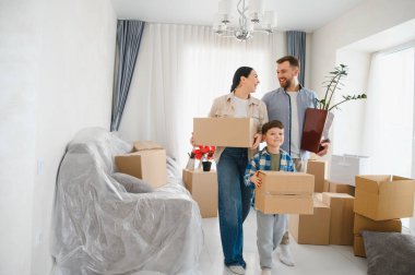 Mutlu bir aile yeni bir eve taşınıyor, karton kutular ve bir bitki taşıyor, paketleri açmaya ve yeni bir hayata başlamaya hazır.