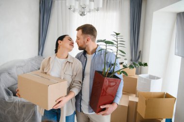 Genç çift taşınma gününü kutluyor, kutuları ve çiçekleri taşıyor, yeni evlerinde birbirlerine bakıyorlar.