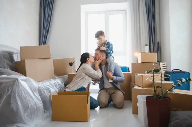 Omuzlarında oğluyla öpüşen aileler, etrafları karton kutularla çevrili, yeni evlerine taşınmalarını kutluyorlar.